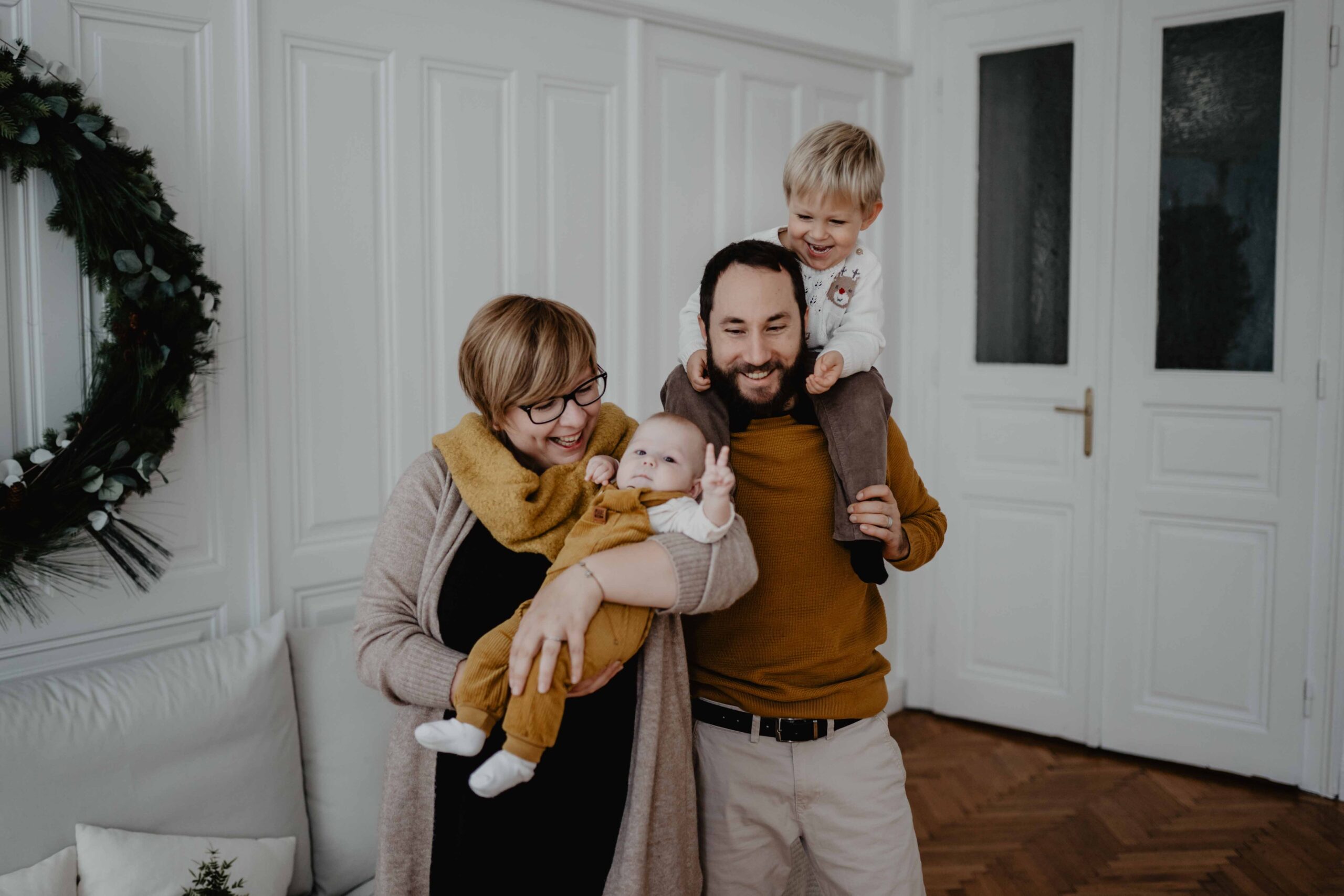 In einem Tageslichtstudio in Wien schaffen wir gemeinsam Familienfotos. Klein A. ist zu dem Zeitpunkt 6 Monate alt und zeigt mit den Fingern ein Peace Zeichen. Die Eltern und der große Bruder lachen.