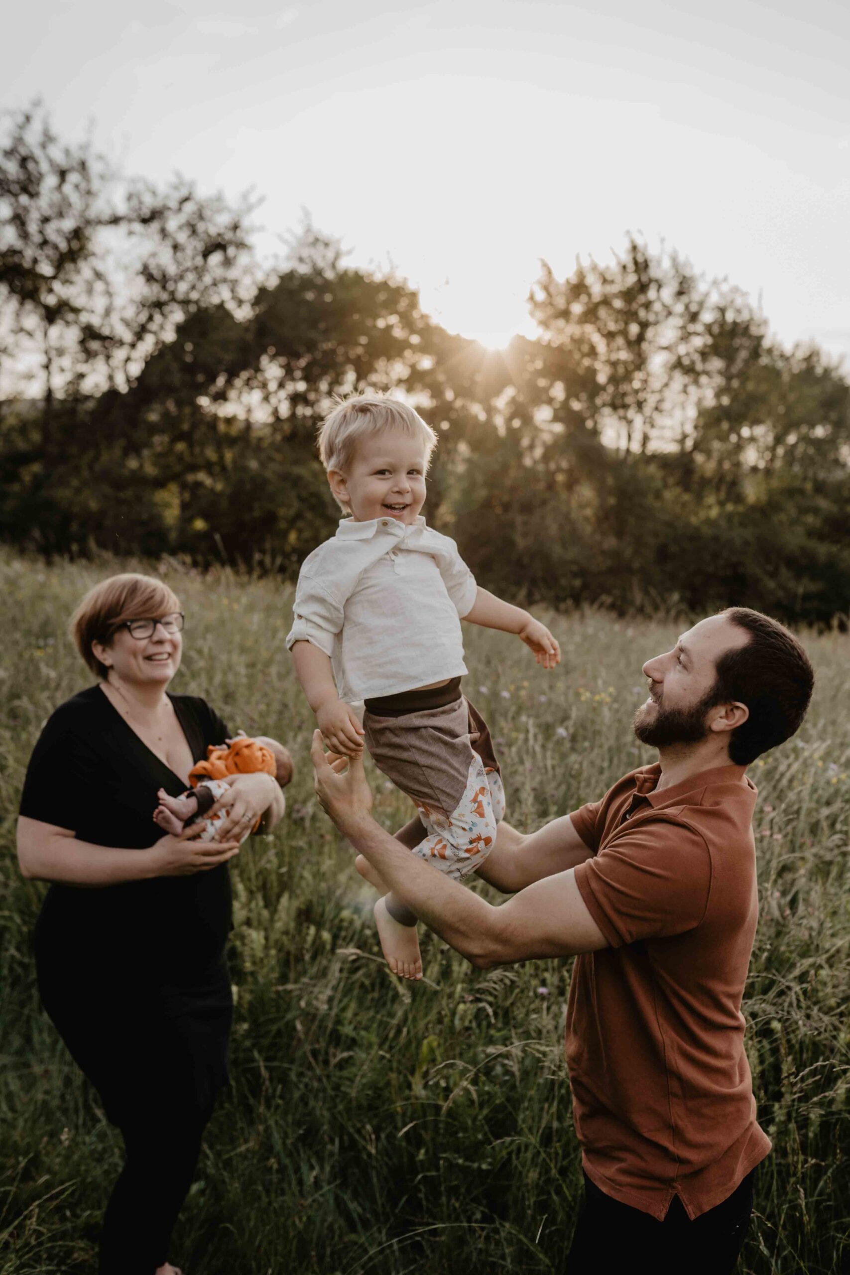 Bei einem Familienfotoshooting in der Natur von Mödling, wirft Papa seinen 3 jährigen Sohn in die Lüfte und Mama hält das Neugeborene. Alle Lachen und haben super viel Spaß.