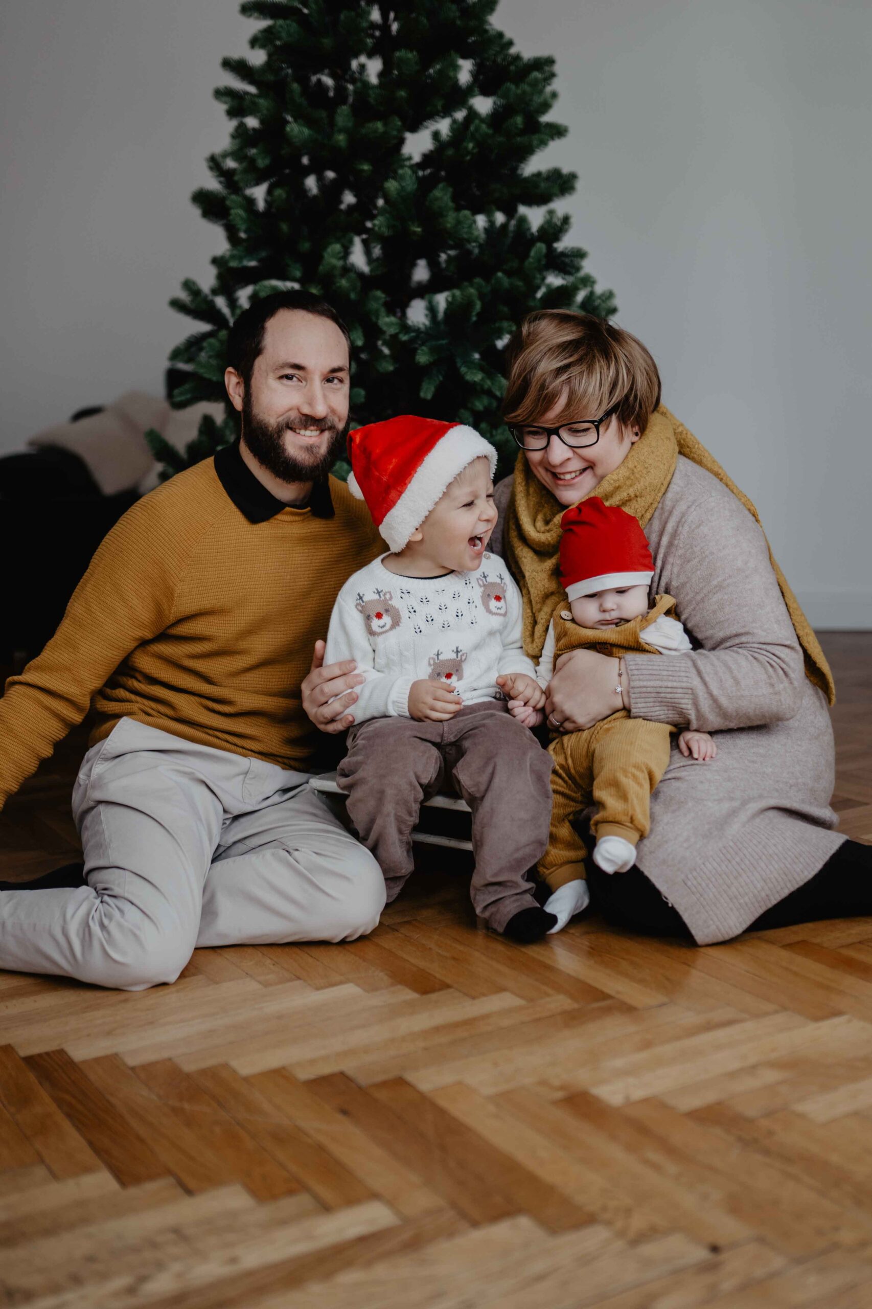 Familie sitzt im Studio bei ihrem Weihnachtsminishooting in Wien am Boden, alle Lachen und die Kinder haben Weihnachtsmützen auf,